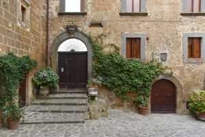 Stone staircase leading to a building in Civita di Bagnoregio, with a decorated doorway and vine-covered walls.