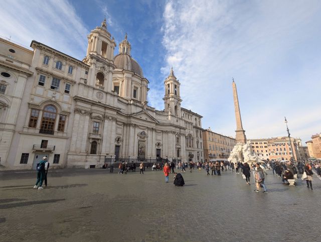 Piazza Navona in Rome, Italy, showcasing the Fountain of the Four Rivers with its obelisk and statues representing the four continents, the church of Sant'Agnese in Agone with its dome and facade, and other Baroque buildings surrounding the piazza.