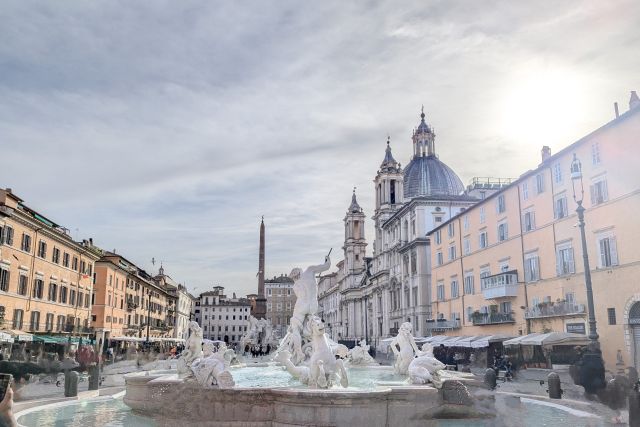 Piazza Navona in Rome, Italy, showcasing the Fountain of the Four Rivers with its obelisk and statues representing the four continents, the church of Sant'Agnese in Agone with its dome and facade, and other Baroque buildings surrounding the piazza.