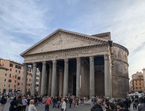 The Pantheon in Rome, Italy, a historic building with a prominent portico of granite columns, featuring an inscription on its architrave, under a cloudy sky.