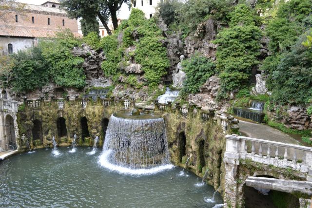 The elaborate water features and gardens of Villa d'Este in Tivoli, Italy, a UNESCO World Heritage Site, showcasing cascading fountains, grottoes, lush vegetation, and the historic villa in the background.